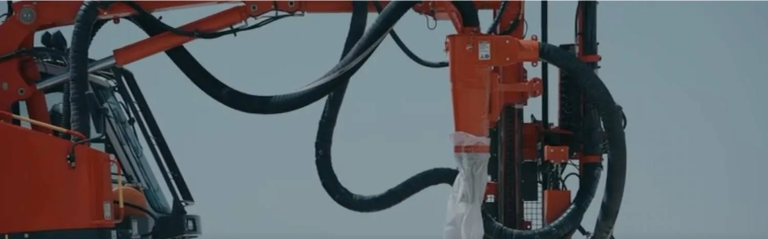 Gros plan sur la tête et les flexibles hydrauliques d'une foreuse orange, mât dressé contre le ciel.