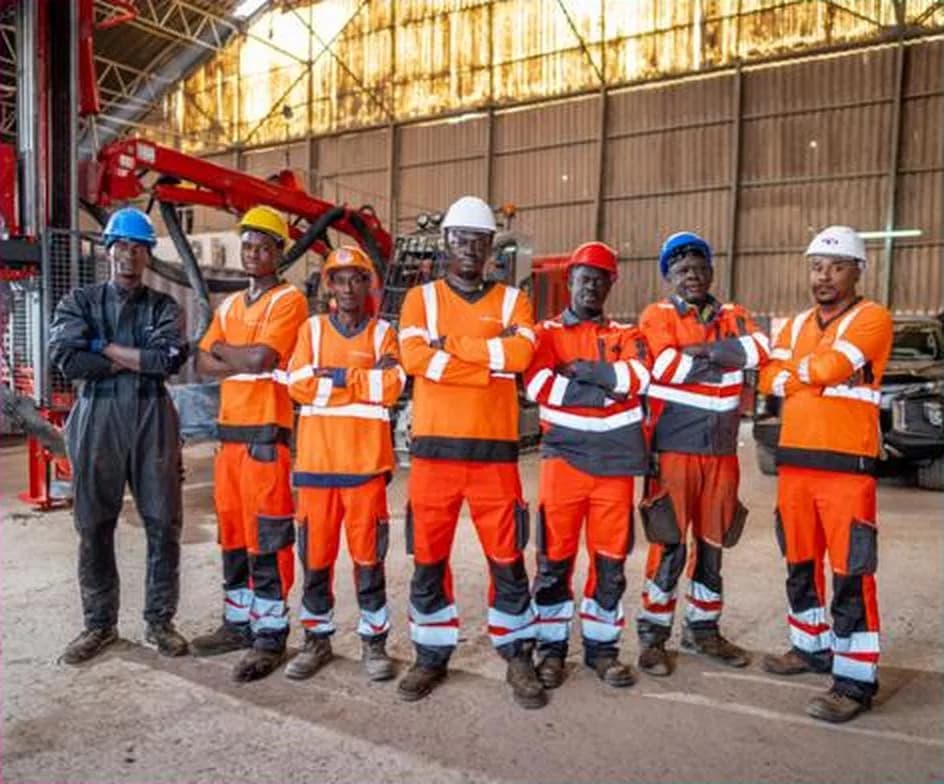 A team of about ten people in high-visibility orange clothing and site helmets, lined up in front of an industrial building.