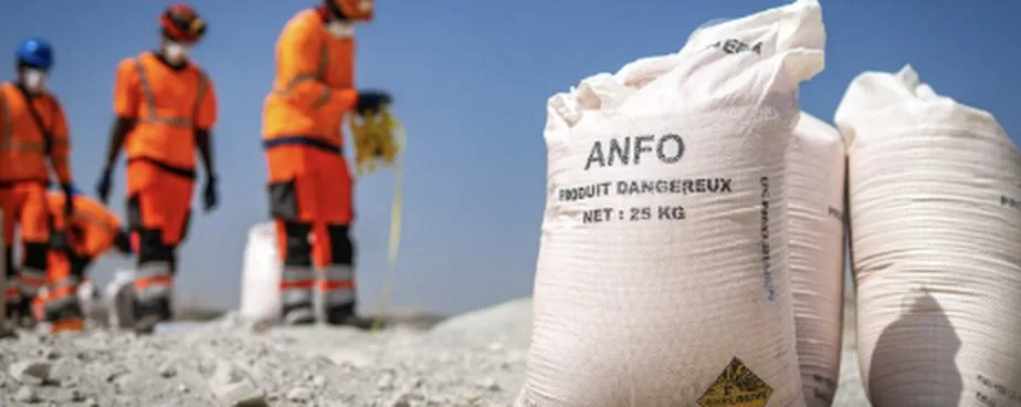 An operator in high-visibility orange clothing draws product from a large white bulk bag on a loading area.